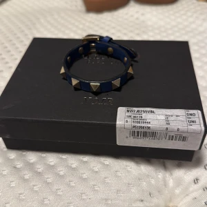 Valentino armband  - Snyggt blått armband från Valentino med coola guldfärgade pyramidnitar och justerbart spänne. Armbandet är gjort i skinn och kommer med originalask, dustbag och äkthetsbevis. Perfekt accessoar för att lyfta din outfit. Helt ok allt som de kom med finns kvar 