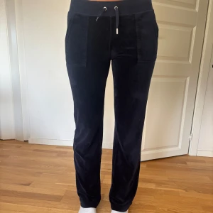 Mörkblå mjukisbyxor med snörning - Mysiga mörkblå mjukisbyxor med snörning i midjan och raka ben. Byxorna har stora fickor fram och bakfickor med knappdetalj. Perfekta för chill dagar eller när du vill vara bekväm men ändå se snygg ut. Det finns en till knapp på högra bak men den syns inte, ena metall grejen är av