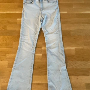 Ljusblå bootcut jeans med hög midja - Snygga ljusblå jeans med bootcut och hög midja. Klassisk femficksmodell med bälteshällor och knappstängning. Jeansen har en rak passform upptill och blir vidare nedtill, vilket ger en cool siluett. Perfekta för dig som gillar retrovibbar och ljusa denimtoner.