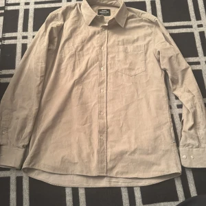 Beige manchester-skjorta Mads Nørgaard - Snygg beige skjorta från Mads Nørgaard i mjuk manchester. Klassisk krage, bröstficka och knappar framtill. Långärmad modell med normal passform, perfekt för dig som gillar stilrena och enkla plagg med lite retro-vibe.