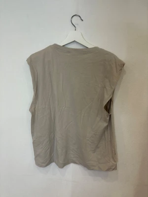 Beige ärmlös linnetopp från H&M - Säljer en enkel och stilren beige linnetopp från H&M. Toppen är ärmlös med rund halsringning och har en loose passform. Materialet är mjuk bomull som känns skönt mot huden. Perfekt för dig som gillar minimalistisk och clean stil.