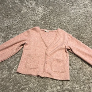 Ljusrosa kofta med v-ringning från Gina Tricot och fickor  - Superfin ljusrosa kofta från Gina Tricot med v-ringad hals och fyra knappar framtill. Koftan har två praktiska fickor på framsidan och är i mjukt bomullsmaterial. Perfekt att slänga på sig när det är lite kyligt ute.