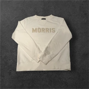 Vit sweatshirt från Morris Gents - Vit sweatshirt från Morris Gents i storlek S. Tröjan har ett broderat MORRIS-tryck framtill och är tillverkad i mjuk bomull. Klassisk rund hals och långa ärmar med ribbade muddar. Perfekt för en chill och stilren look.
