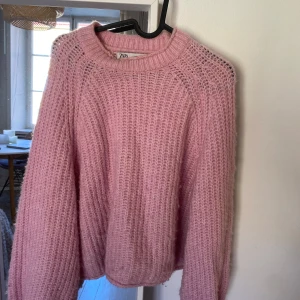 Rosa stickad tröja från Zara - Mysig rosa stickad tröja från Zara med grovstickat mönster och rund halsringning. Tröjan har lång ärm och en avslappnad passform, perfekt för kyliga dagar. Superfin färg som lyfter vilken outfit som helst!
