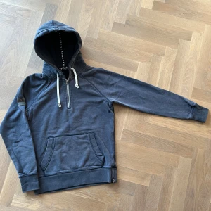 Unik Superdry hoodie/ M, men passar S - Snygg marinblå hoodie från Superdry med huva och vita snören. Tröjan har en half zip-dragkedja framtill, vilket gör tröjan unik och svår att hitta. Framtill är det en klassisk hoodieficka. Materialet är mjuk bomull och passformen är liten för M, passar bättre som S. Perfekt för chill dagar och streetwear.