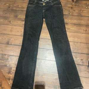 mörkgrå bootcut jeans från Vero Moda - Svarta jeans från Vero Moda i modellen Atom Jeans med bootcut-snitt. Snygga kontrastsömmar i gult och klassisk femficksdesign. Jeansen har normal passform och är tillverkade i jeansmaterial. Perfekt för dig som gillar retrovibbar och vill ha ett coolt statement. 