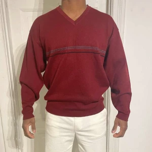 Vinröd stickad tröja från Wolsey XL - Vinröd stickad tröja från Wolsey i storlek XL. Tröjan har v-ringning, diskreta ränder över bröstet i grått och blått samt långa ärmar. Perfekt för dig som gillar klassisk stil med en twist. Materialet är mjukt och skönt, passar till många outfits.