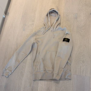 Beige hoodie från Stone Island - Säljer en beige hoodie från Stone Island med klassisk patch på vänster ärm. Köpte ny på NK för 2500kr. Tröjan har huva med snörning, magficka och ribbade muddar. 
