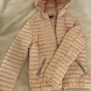 Ljusrosa pufferjacka från Colmar - Snygg ljusrosa pufferjacka från Colmar Originals med quiltad design och huva. Jackan har två fickor med dragkedja och en stilren look som passar perfekt till höst och vinter. Lätt och smidig att bära, med långärmade ärmar och hel dragkedja framtill. Jättesnygg och trendig!!💕💕Passar en S