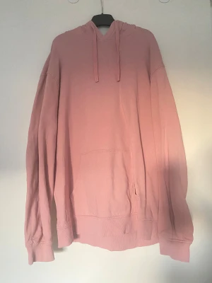 Ljusrosa hoodie i ekologisk bomull - Säljer en ljusrosa hoodie från Cubus i ekologisk bomull. Tröjan har huva med snörning, stor magficka och långa ärmar med ribbade muddar. 