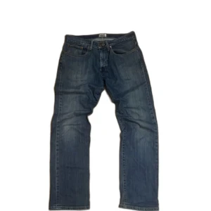 Blå jeans Grant Regular Fit 34/32 - Snygga blå jeans från Grant i modellen Regular Fit, storlek 34/32. Klassisk femficksdesign med raka ben och normal passform. Jeansen har en cool vintage-wash och detaljer som läderpatch bak i midjan. Perfekt för dig som gillar tidlös stil och bekväma jeans.