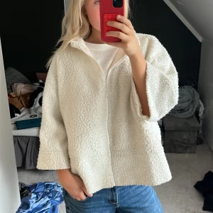 Vit teddyjacka med dragkedja - Mysig vit teddyjacka med krage och dragkedja framtill. Jackan har en oversized passform och är tillverkad i fluffigt teddy-material. Perfekt för lager-på-lager och chill vibes. Ärmarna är lite kortare för en avslappnad look.