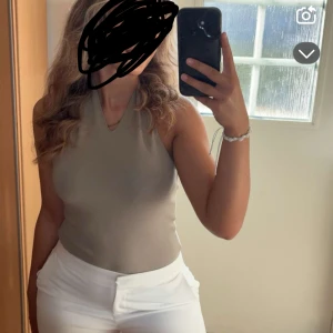 Beige halterneck body  med v-ringning - Säljer en stilren beige string body med v-ringad hals och ärmlös design. Toppen har en tight passform och är tillverkad i mjukt bomullsmaterial som känns skönt mot huden. Perfekt för varma dagar och enkel att matcha med dina favoritjeans eller kjol. Knappt använd.