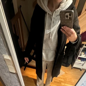 Svart kappa med bälte och fickor - Säljer en svart kappa med klassisk krage och stora fickor framtill. Jackan har ett bälte i midjan för extra stilpoäng och är lång i modellen. Materialet känns som ull och passformen är loose, perfekt för lager-på-lager. Snygg och enkel att matcha med hoodies eller jeans. Jag är 163 cm lång för referens. Kappan är lite nopprig men inget som störs av synen 
