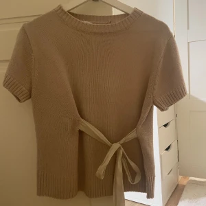 Populär Zara topp - Superfin beige stickad topp med korta ärmar och ribbade muddar. Snygg detalj med knytband i midjan som ger en extra touch. Perfekt till jeans eller kjol för en chill och trendig look.