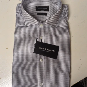 Skjorta från Bruun & Stengade prislappen kvar - Snygg rutig skjorta från Bruun & Stengade i modern fit. Skjortan har klassisk krage, vita knappar och ett diskret rutmönster i grått och vitt. Materialet är mjukt och lättskött bomull, perfekt för dig som gillar stilren och clean look.