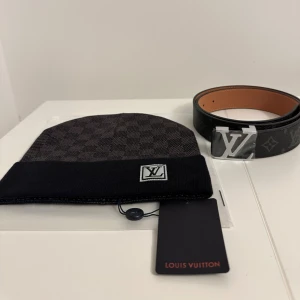 Svart rutig mössa L.V - Snygg svart mössa L.V med klassiskt rutigt mönster och uppvikt kant. Mössan har en stilren L.V-logga framtill och är tillverkad i mjukt material som känns lyxigt. Perfekt för dig som vill ha en exklusiv accessoar med street vibe.