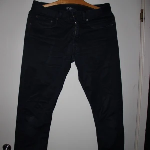 Polo Ralph Lauren jeans - Snygga svarta byxor från Polo Ralph Lauren med klassisk femficksdesign och dragkedja. Byxorna har raka ben och är tillverkade i ett mjukt bomullsmaterial som ger en clean och stilren look. Perfekta för dig som gillar tidlös stil.