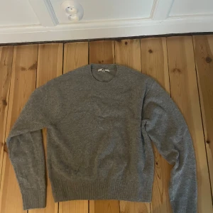 Grå stickad tröja från Uniqlo XS - Snygg grå stickad tröja från Uniqlo i storlek XS. Tröjan har rund hals, ribbade muddar vid ärmslut och nederkant samt långärmad passform. Perfekt för dig som gillar enkel och stilren design med mjukt material.