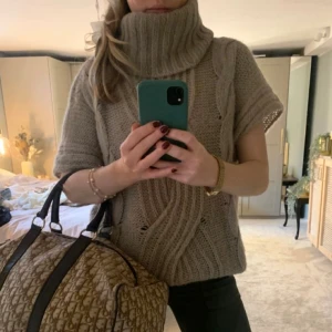 Beige stickad polotröja Benetton - Säljer en beige stickad polotröja från Benetton med bred, ribbad krage och korta ärmar. Tröjan har snygga kabelstickade detaljer framtill och är loose fit. Passar även S