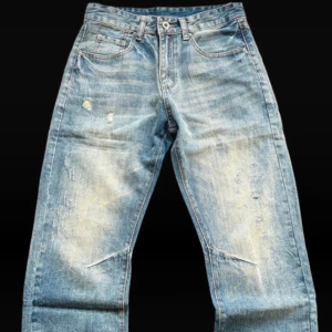 Blå slitna bootcut jeans - Säljer ett par blå jeans med bootcut passform och slitna detaljer på benen från pieces of life studio. Jeansen har en ljus tvätt med tydliga slitningar och små hål för en cool, avslappnad look.