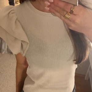 Ribbad vit topp med puffärm - Säljer en ribbad vit topp med rund hals och stora puffärmar som ger en extra cool touch. Materialet är mjukt och stretchigt, perfekt för dig som gillar att sticka ut lite. Passformen är slim och toppen är riktigt snygg till både jeans och kjol.