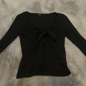Svart långärmad knytblus - Svart långärmad blus från Gina tricot med snygg knytning framtill. Toppen har en djupare v-ringning och är figurnära i modellen. Perfekt att styla med jeans eller kjol för en trendig look.