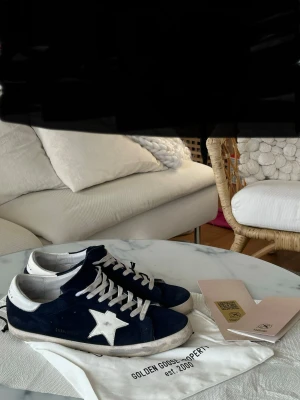 Golden Goose mörkblå sneakers med stjärna - Säljer ett par snygga Golden Goose sneakers i mörkblå mocka med vit stjärndetalj på sidan och vita snören. Storlek 45 men sitter som 44. Skorna har rund tå, platt sula och vit häl. Medföljer originalpåse och papper. Perfekta för dig som gillar coola och unika sneakers.