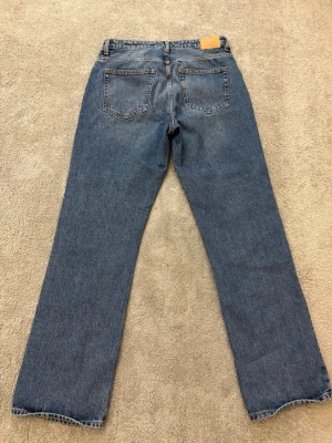 Blå jeans straight fit - Klassiska jeans i mörkblå tvätt med rak passform och hög midja. Jeansen har fem fickor, knappgylf och robust denimkänsla. Perfekt för dig som gillar tidlös stil och vill ha ett par jeans som funkar till allt.