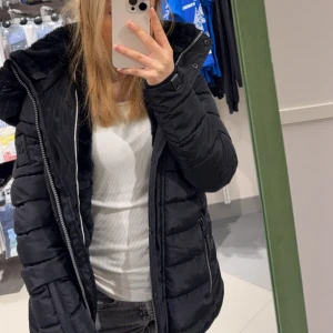 Svart vinterjacka från Navahoo – varm, stilren & mjuk! - Snygg och figursydd vinterjacka från Navahoo, perfekt för kalla dagar! Jackan har en mjuk fuskpälsfodrad huva och insida som håller dig varm och bekväm. Tillverkad i vattenavvisande material, med dragkedja och knappar framtill för extra skydd mot kyla. Färg: Svart Märke: Navahoo Storlek: XS Fuskpälsfoder i huva och insida Flera fickor med dragkedja och knappar Figursydd passform Perfekt för höst & vinter  I mycket fint skick – använd få gånger! Passar dig som vill ha varm, trendig och bekväm 