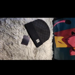 Svart mössa - Snygg svart mössa med klassisk  framtill. Mössan har en stilren design med uppvikt kant och diskret mönster. Perfekt för dig som vill ha en lyxig och trendig accessoar till vintern.