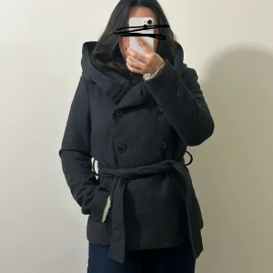 Mörkgrå kappa med luva och bälte - Snygg mörkgrå kappa med stor luva och knytbälte i midjan. Liten i storleken , står L men är mer som en XS, jag som är S sitter den lite tajt. Som ny. Skriv om flera bilder önskas 🥰