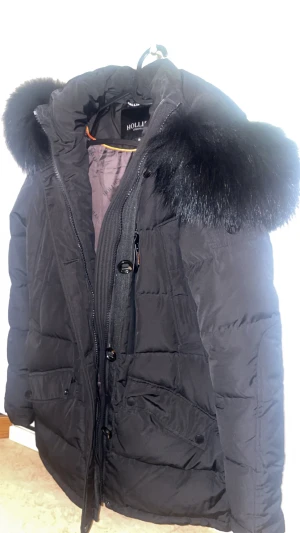 Svart vinterjacka med äkta päls från Hollies - Svart Hollies vinterjacka med äkta päls, i nyskick!  Använd endast 1 gång – ser helt ny ut. Stilren, varm och exklusiv modell som passar perfekt för vintern.  Kontakta mig gärna vid intresse för fler bilder!   Storlek: 34 Nypris: 5500  Mitt pris: 2500
