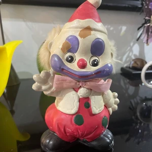 Clown vintage  - Denna produkt är en vintage clown-sparbössa i keramik med färgglad målning . Viss färgslitage och mindre repor syns, men den är i överlag gott skick. Perfekt som retro inredningsdetalj eller samlarobjekt.