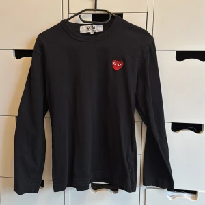 Svart långärmad tröja Comme des Garçons strl S - Svart långärmad tröja från Comme des Garçons Play i storlek S. Tröjan har ett ikoniskt rött hjärta med ögon broderat på bröstet. Rund hals och mjuk bomull gör den skön att bära. Perfekt för dig som gillar stilrena plagg. Sonen som är 15 år har precis vuxit ur den. 