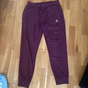  Beverly Hills Polo Club mjukisbyxor  - Snygga vinröda mjukisbyxor från Beverly Hills Polo Club med broderad logga på framsidan. Byxorna har snörning i midjan, muddar vid bensluten och en bakficka. Perfekta för chill eller häng med kompisar.