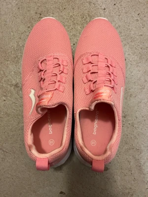 Rosa sneakers från Bagheera strl 38 - Snygga rosa sneakers från Bagheera i storlek 38. Skorna har en stickad ovandel i syntetmaterial, elastisk snörning och vit platt sula med rosa detaljer undertill. Perfekt för dig som gillar sportig och fräsch stil. Lätta och bekväma att bära.
