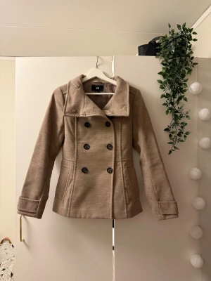 Beige skepparkavaj från H&M - Snygg beige kort kappa från H&M med dubbelknäppning och högt krage som kan bäras uppvikt eller nedvikt! 🤍