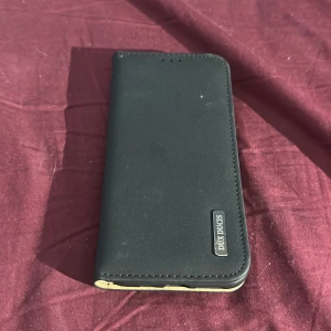 Dux Ducis Plånboksfodral för iPhone - Elegant svart plånboksfodral från Dux Ducis, kompatibelt med iPhone 11 Pro. Fodralet har plats för kort och skyddar både fram- och baksida. Mindre yttre slitage syns, men i gott skick och redo att användas för att ge din mobil ett stilrent skydd.