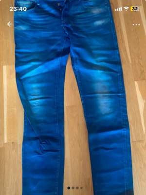 G-Star Raw 3301 blå jeans W38 L38 - Snygga blå jeans från G-Star Raw, modell 3301. De har klassisk femficksdesign, raka ben och kontrastsömmar. Jeansen är i en intensiv blå färg med detaljer. Perfekt för dig som gillar streetstyle och vill ha ett par jeans med attityd.