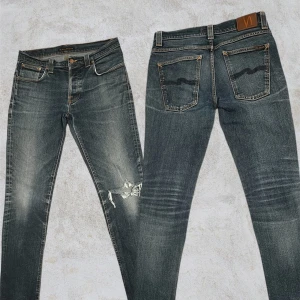 Mörkblå  jeans från Nudie - Mörkblå skinny jeans från Nudie med slitningar på knät och fransade benslut. Klassisk femficksmodell med orangea sömmar och Nudie-logga på bakfickan. Jeansen har en snygg tvätt och är tillverkade i stretchig denim för skön passform. Köpta för cirka 10 års sedan Grim trim selvge väldigt unika och använda 