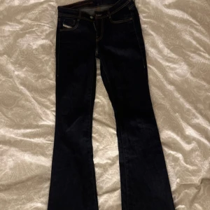 Mörkblå bootcut jeans från Diesel - Snygga mörkblå jeans från Diesel med klassisk bootcut passform och kontrasterande gula sömmar. Modellen har fem fickor, dragkedja och knapp framtill samt Diesel Industry-märke bak på linningen. Perfekt för dig som gillar stilrena jeans med lite extra edge. Aldrig använda på grund av för liten storlek. 