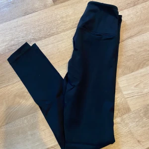 Svarta lumi tights från Relode  - Säljer ett par svarta lumi tights från Relode med hög midja och tight passform. Materialet är mjukt och stretchigt, perfekt för träning eller chill. Diskret logga på benet. Snygg och enkel design som sitter skönt hela dagen. Nypris 699kr