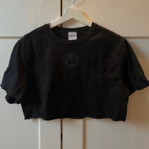 Svart croppad topp från Gymshark - Svart croppad topp från Gymshark med rund halsringning och korta ärmar. Toppen har en diskret Gymshark-logga framtill och är tillverkad i mjuk bomull, perfekt för en sportig och avslappnad stil.