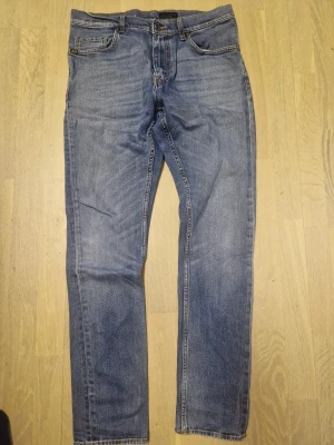 Blå Tiger jeans Pistolero 33/34 straight fit - Snygga blå jeans från Tiger Modell Pistolero W33/L34i klassisk straight fit med fem fickor och orangea sömmar. Jeansen har normal passform och är tillverkade i slitstarkt denim. Perfekt för dig som gillar en enkel och tidlös look.