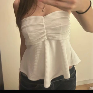 Vit tubtopp - Säljer en vit tubtopp med ribbad struktur och snygg rynkning framtill. Toppen har en liten slits baktill för extra detalj. Köpt i Thailand. 