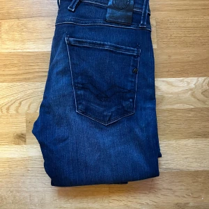 Replay Anbass jeans mörkblå, stl 28 - Snygga Replay Anbass jeans i mörkblå tvätt med klassiska femficksdetaljer och diskret slitning. Jeansen har rak passform och är tillverkade i mjukt denimtyg som sitter skönt hela dagen. Perfekta för dig som gillar stilrena och tidlösa jeans. Riktigt bra skick. Kontakta mig vid minsta fundering   