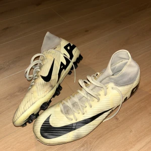 Nike fotbollsskor i beige och svart - Säljer ett par beige Nike fotbollsskor med svart swoosh och snörning. Skorna har en strumpliknande hög krage och platt sula med fasta dobbar för bra grepp. Storlek 46, inget som är sönder/trasig eller liknande med skorna