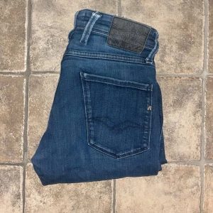 Replay Anbass jeans  - Snygga Replay Anbass jeans i mörkblå tvätt med klassisk femficksdesign och svarta detaljer på bakfickan. Modellen är slim fit med smal passform och stretchigt jeanstyg för extra komfort. Längd 95cn, midja 38cm.  JAG SKICKAR EJ FLER BILDER NÄR JAG BÄR JEANSEN! för storleksguide hänvisar jag till måtten och för bättre inblick i passformen rekommenderar jag att googla på modellnamnet. :) S4