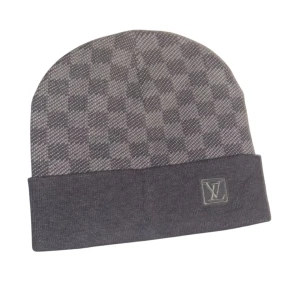 Iv grå rutig mössa - Exklusiv grå mössa från Louis Iv med klassiskt rutigt mönster och Iv-logga framtill. Mössan har uppvikt kant och är tillverkad i mjukt ullmaterial som känns lyxigt och bekvämt. Perfekt för dig som vill ha en stilren och trendig accessoar.